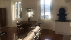 A room with a dining table, chairs, a sofa, a large mirror, and a window with a view of the outside. - Apartment (nice)