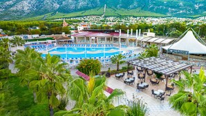 A resort with a swimming pool, outdoor seating, and a view of a mountainous town. - Sahra Su Holiday Village & SPA (Fethiye)