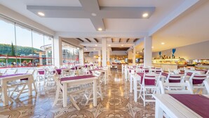 A spacious restaurant with white tables and chairs, large windows, and a view of the outdoors. - Sahra Su Holiday Village & SPA (Fethiye)