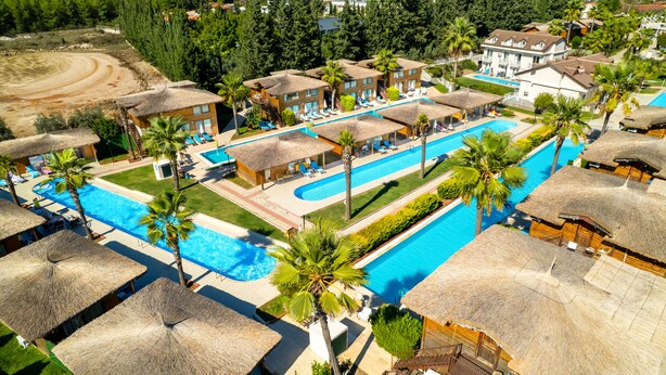 A resort with multiple swimming pools, thatched-roof structures, and palm trees. - Sahra Su Holiday Village & SPA (Fethiye)