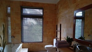 A bathroom with a bathtub, toilet, and sink. There are windows with blinds, a mirror, and a plant. - Just outside Ubud, peaceful 3BR Villa with rice field views. (Tampaksiring, Gianyar Regency)