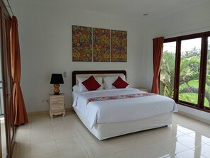 A bedroom with a large bed, a nightstand with a lamp, a window with curtains, and a wall with three paintings.