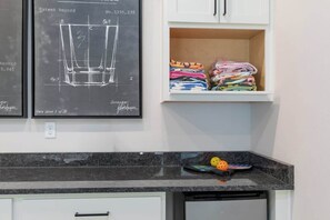 A kitchen with a marble countertop, a dishwasher, and a shelf with folded clothes.