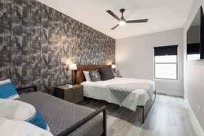 A bedroom with two beds, a ceiling fan, bedside lamps, and a window with blinds.