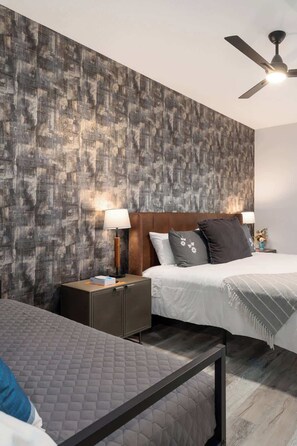 Une chambre d’hôtel au design moderne, dotée d’un grand lit avec une tête de lit en bois, d’une table de chevet avec une lampe et d’un ventilateur de plafond.