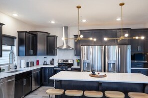 A modern kitchen with dark cabinetry, stainless steel appliances, and a central island with stools. - 10-Bedroom Lakeside Lodge with Indoor Pool, Sleeps 34, Near Table Rock Lake (Hollister)