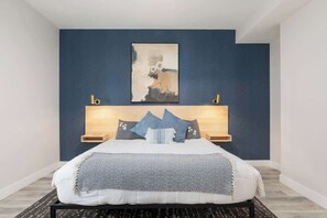 A bedroom with a bed, a headboard, bedside tables, and a wall-mounted artwork.