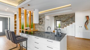 A modern kitchen with a central island, white cabinetry, and a wooden staircase in the background. - Oasis of peace, with wellness, playground, pool, barbecue (Mofardini)