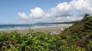 A beach with waves, a clear sky, and greenery in the foreground. - Salt Loft - Oceanfront, Hot Tub and Firepit! (Ucluelet)