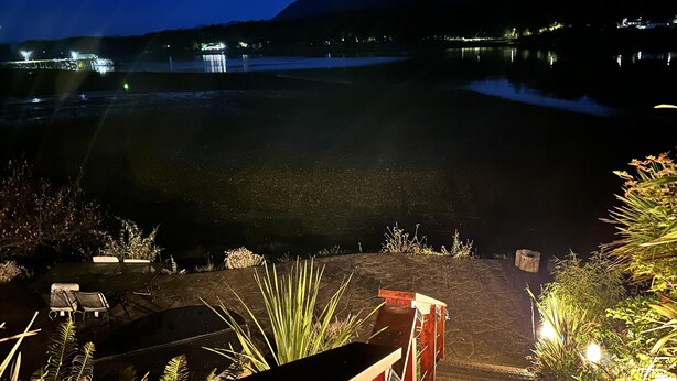 A nighttime view of a lakeside area with a wooden staircase leading down to a dock, surrounded by vegetation. - Salt Loft - Oceanfront, Hot Tub and Firepit! (Ucluelet)