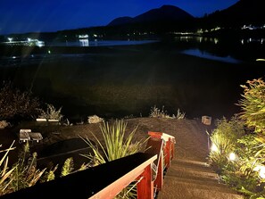 A nighttime view of a lakeside area with a wooden staircase leading down to a dock, surrounded by vegetation. - Salt Loft - Oceanfront, Hot Tub and Firepit! (Ucluelet)