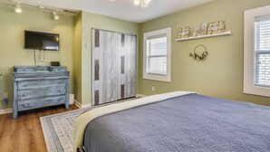 A bedroom with a bed, dresser, TV, and a ceiling fan. - A Bended Oak Bungalow by Ryson Vacation Rentals (Galveston)