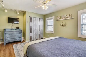 A bedroom with a bed, dresser, TV, and a ceiling fan. - A Bended Oak Bungalow by Ryson Vacation Rentals (Galveston)