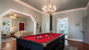 A pool table in a room with a chandelier, a red door, and a view to a powder room. - A Bended Oak Bungalow by Ryson Vacation Rentals (Galveston)