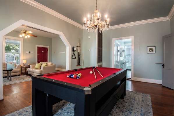 A pool table in a room with a chandelier, a red door, and a view to a powder room.