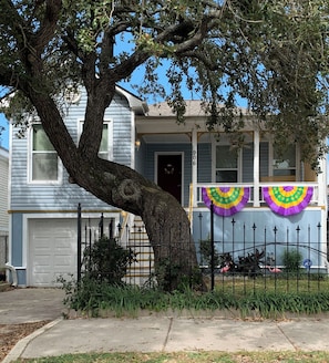 A two-story house with a large tree in front, a garage, and a front porch with colorful decorations.