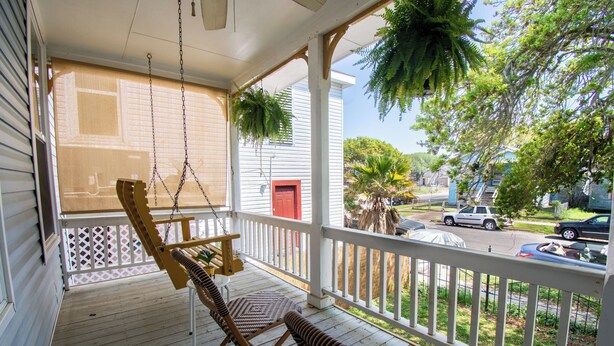 A porch with a swing chair, a bench, and hanging plants. - A Bended Oak Bungalow by Ryson Vacation Rentals (Galveston)