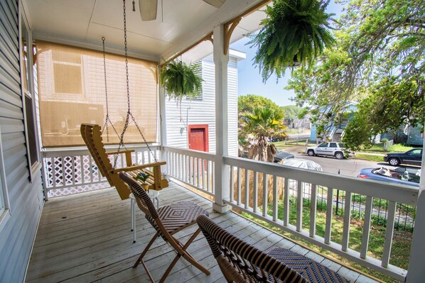 A porch with two wicker chairs, a swing, and hanging plants.