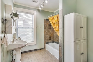 A bathroom with a pedestal sink, a mirror, a bathtub, and a shower curtain.