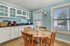 A kitchen with white cabinets, a dining table with placemats, and a fan near the window.