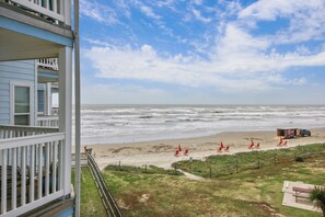 A beach view from a balcony with a view of the ocean, beach chairs, and a truck. - Pineapple Paradise by Ryson Vacation Rentals (Galveston)