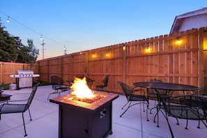 A backyard with a fire pit, outdoor seating, and a grill.