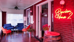Ein gemütliches Zimmer mit einem Neon-Schild, das "Bourbon House 2" zeigt, einem Deckenventilator und einer Ziegelwand.