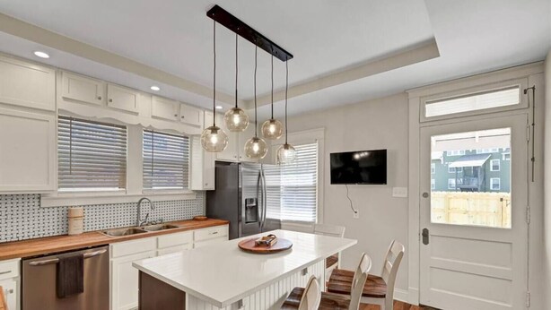Eine moderne Küche mit weißen Schränken, einem Edelstahlkühlschrank, einem eingebauten Ofen, einer großen Kochinsel mit Holz Arbeitsplatte und einem Essbereich mit weißen Stühlen.