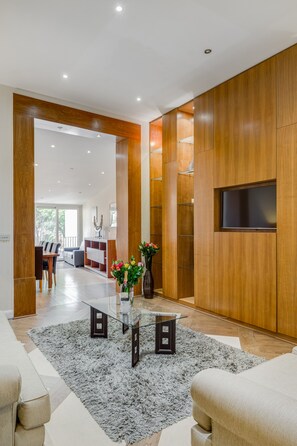 Una sala de estar moderna con una mesa de centro de vidrio, un tapete gris, paredes de madera y un televisor montado en la pared.