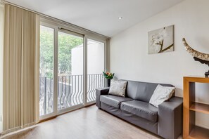 Ein modernes Wohnzimmer mit einem grauen Sofa, einem Holztisch und einem großen Fenster mit Blick ins Grüne.