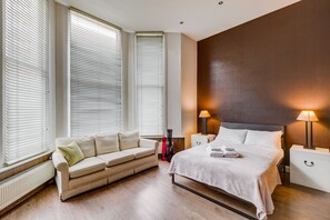 Ein modernes Schlafzimmer mit einem Bett, einem Sofa und einem Nachttisch mit Lampen.