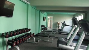 Une salle de sport équipée de tapis de course, d’haltères et d’un téléviseur fixé au mur.