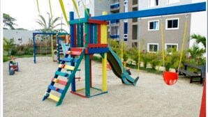 Un terrain de jeux équipé d’un toboggan et de structures d’escalade, entouré d’un bâtiment doté de nombreuses fenêtres et de balcons.