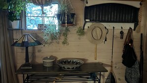 A rustic cabin interior with a wooden table, hanging plants, a woven basket, and a wall-mounted rack with bags and a hat. - Cooperstown Lake Cabin Million Dollar Views (Cooperstown)