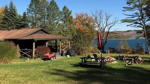 A rustic cabin with a covered porch, picnic tables, and a view of a lake. - Cooperstown Lake Cabin Million Dollar Views (Cooperstown)