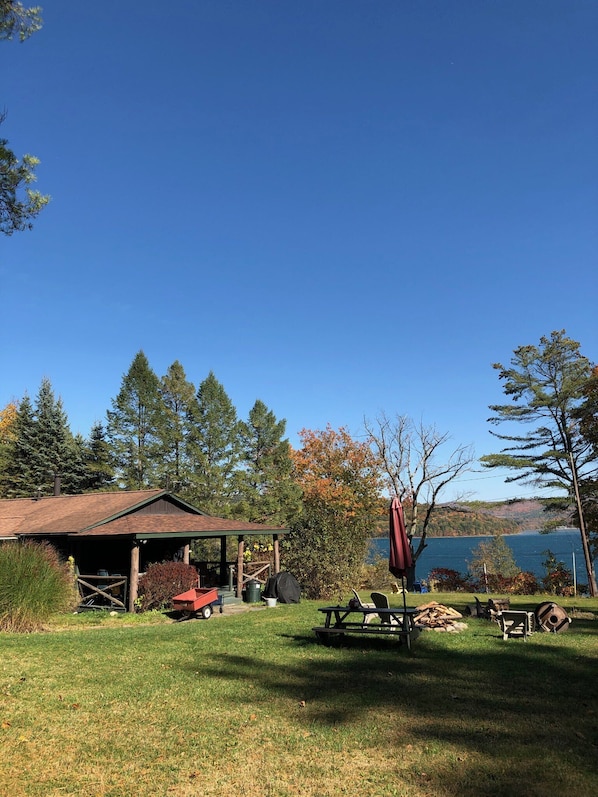 Una cabaña rústica con un porche cubierto, mesas de picnic y vistas a un lago.