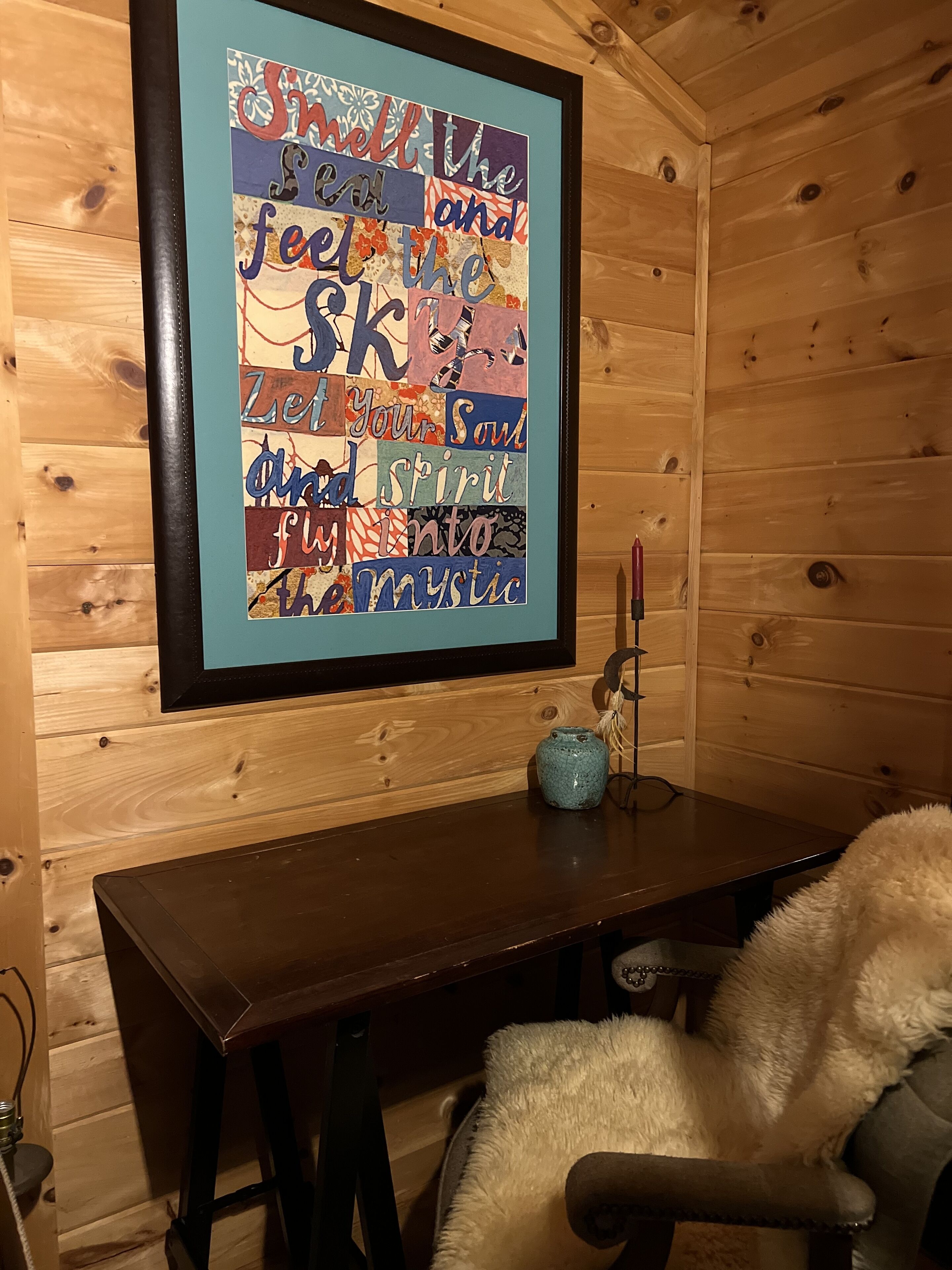 Een gezellig interieur van een blokhut, met een houten wand, een lijstwerk met kunst, een tafeltje en een zachte fauteuil.