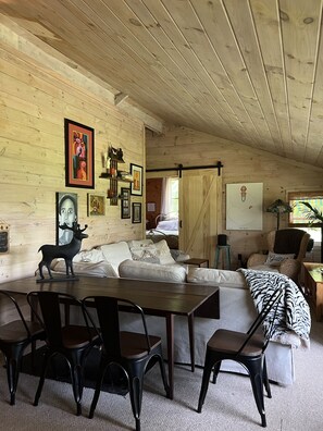 Interior acogedor de una cabaña con techo de madera, una mesa de comedor con sillas, un sofá y varias obras de arte enmarcadas en las paredes.