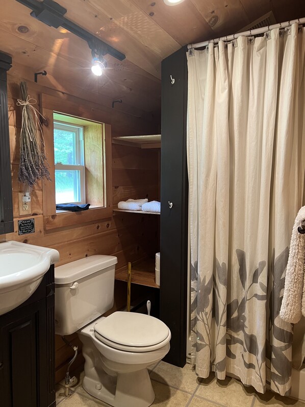 A wooden cabin bathroom with a toilet, sink, and window. - Cooperstown Lake Cabin Million Dollar Views (Cooperstown)