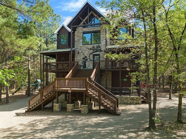 Un chalet doté d’une façade en pierre, d’une terrasse en bois et d’un escalier menant à un balcon.