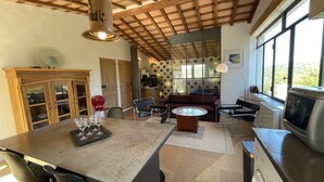 A spacious kitchen with a central island, a dining area with chairs, a sofa, and a large window providing a view of the outdoors. - Loft at the foot of the Ventoux with swimming pool, jacuzzi and balneotherapy. (Mollans-sur-Ouvèze)