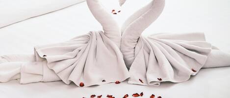 Uma cama com arranjo de toalhas em formato de dois cisnes e um coração feito de pétalas de rosa.