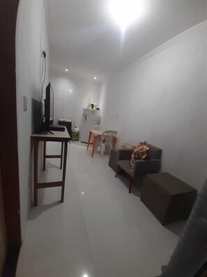 A compact living space with a dining area, a sofa, a small table, and a kitchenette in the background.