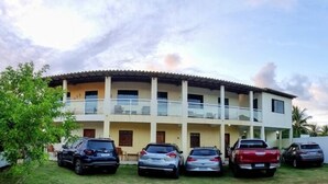 Un edificio de varios pisos con techo plano y balcones. Hay varios coches aparcados adelante.