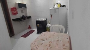 Una cocina compacta con azulejos blancos, un refrigerador, un microondas y un pequeño comedor con una mesa y una silla.