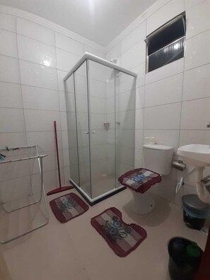 Un baño con cabina de ducha de vidrio, inodoro, lavabo y una pequeña alfombra.