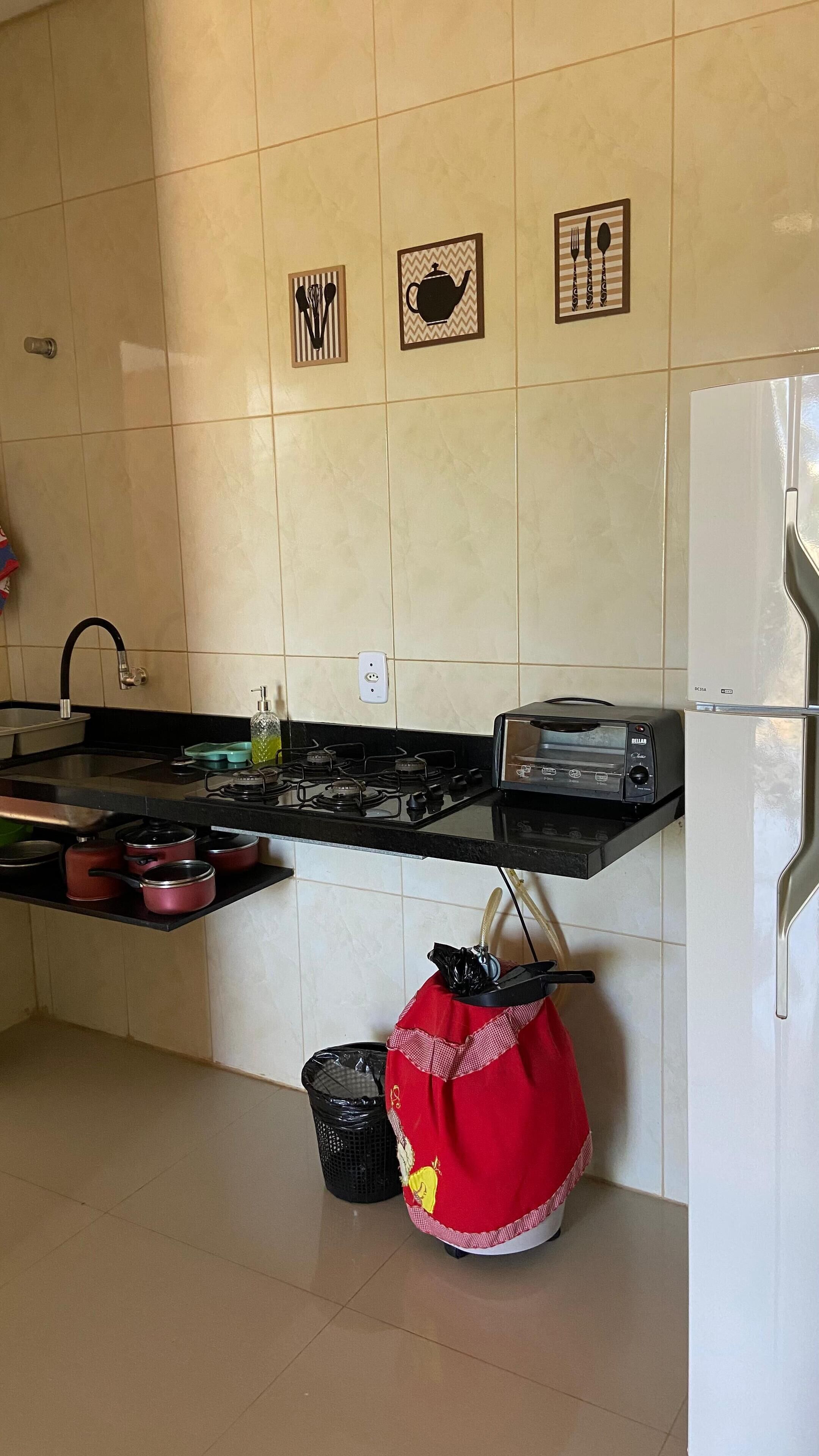 Une cuisine équipée d’une cuisinière, d’un évier et d’un réfrigérateur. Des éléments décoratifs ornent le mur au-dessus du plan de travail.
