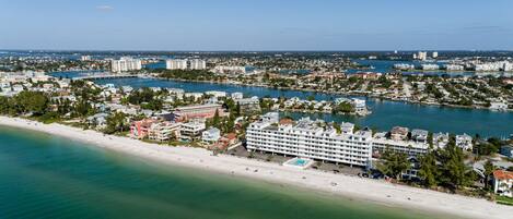 An aerial view of a coastal city with a prominent hotel featuring multiple floors and a swimming pool.