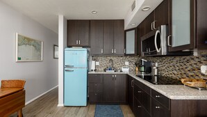 A compact kitchen with dark wood cabinets, a blue refrigerator, a tiled backsplash, and a granite countertop. - Sunset Beach Condo (Treasure Island)