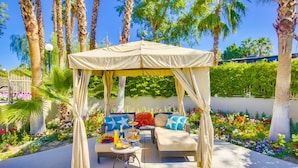 An outdoor seating area with a canopy, cushioned sofas, and a table with food and drinks. - The Villas at Emerald Desert RV Resort (Palm Desert)